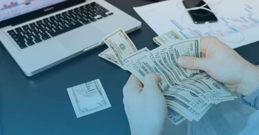 Person counting money that has money scattered over desk and seems disorganized