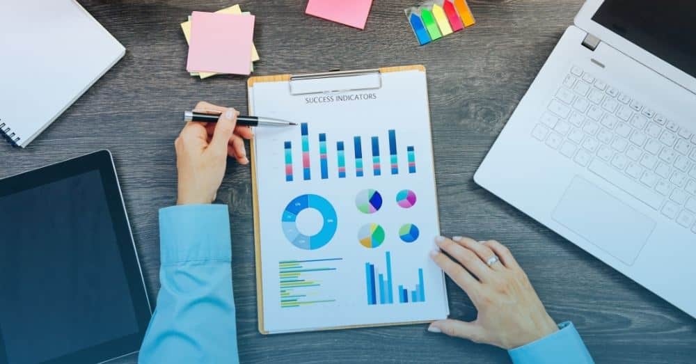 Person holding pen and reviewing a clipboard with financial health indicators at a desk.