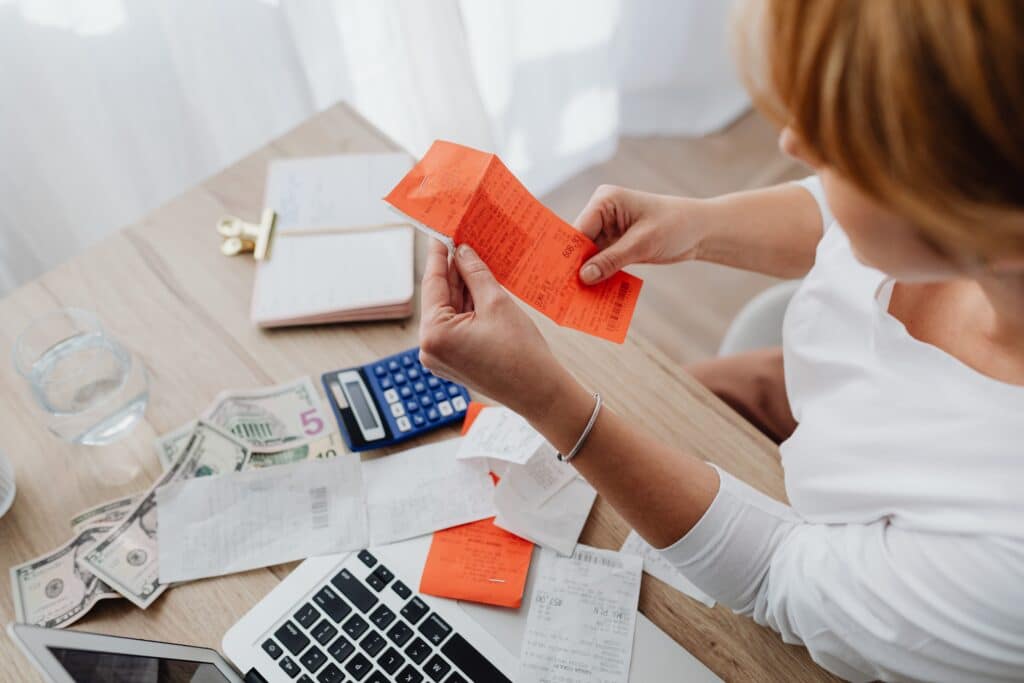 woman looking at receipt with laptop, calculator and papers on a desk around her