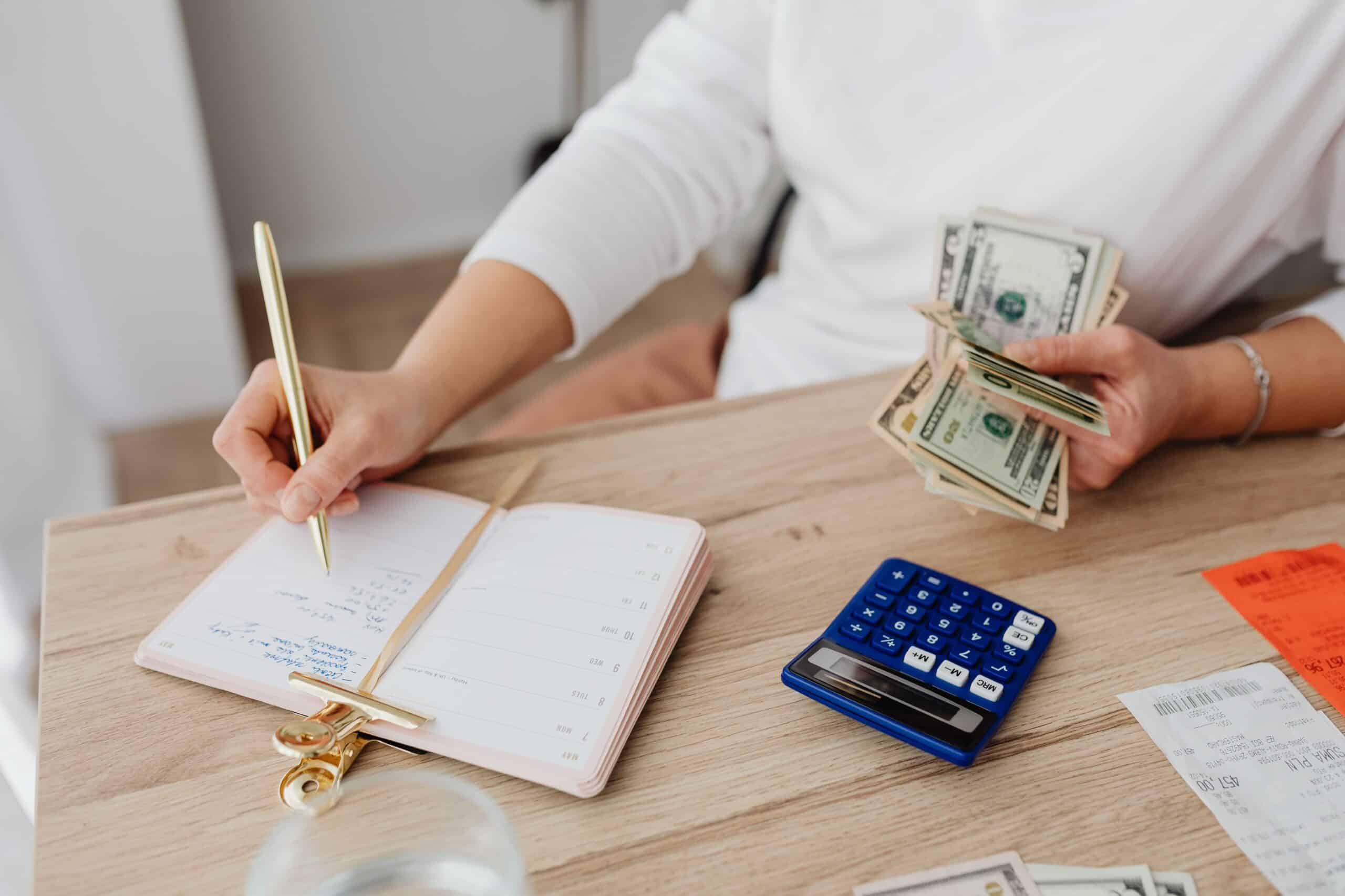 small business owner budgeting by writing in a notebook and counting money with a calculator